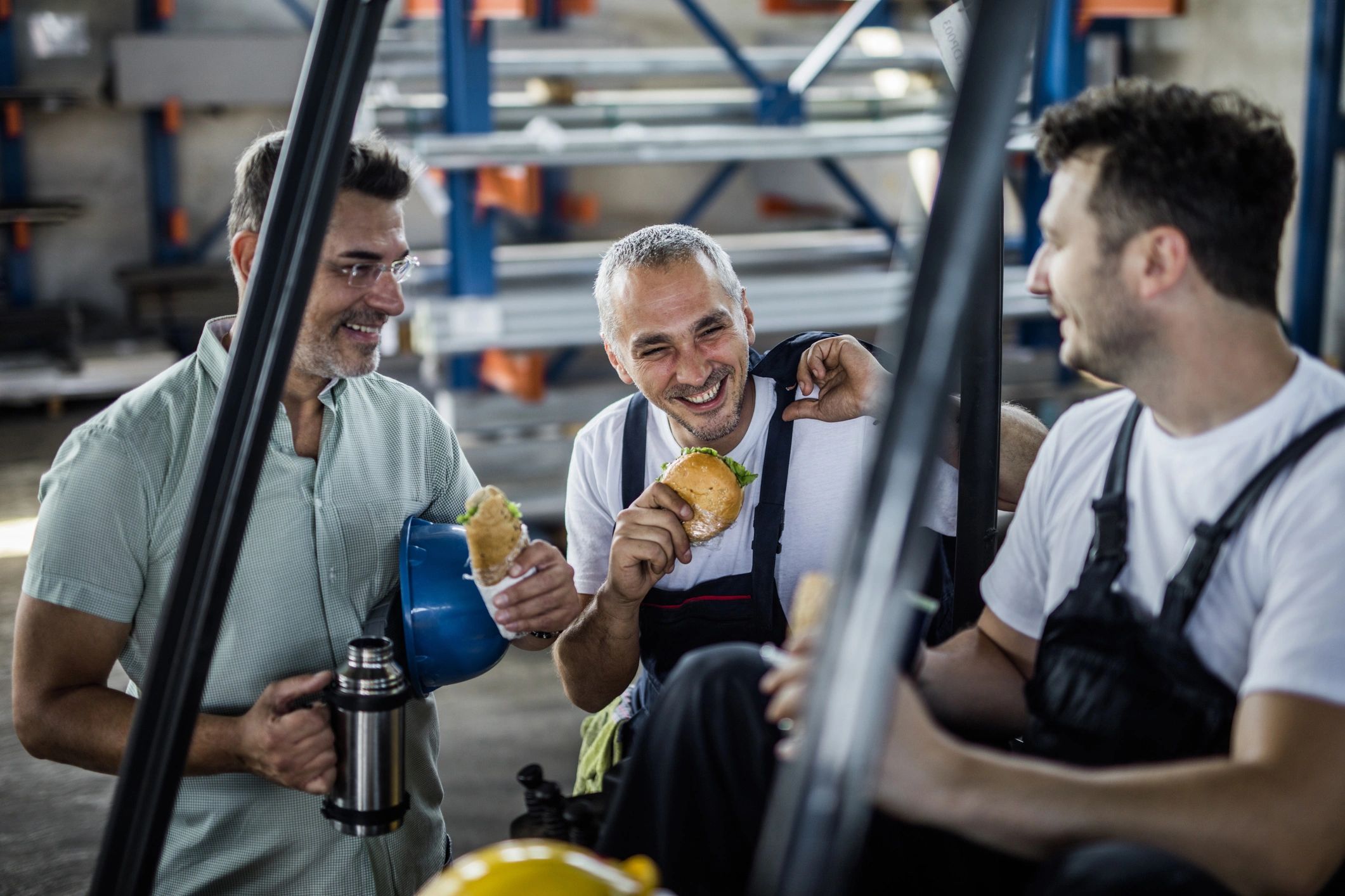 Trades workers and their manager talking over lunch in a factory break area