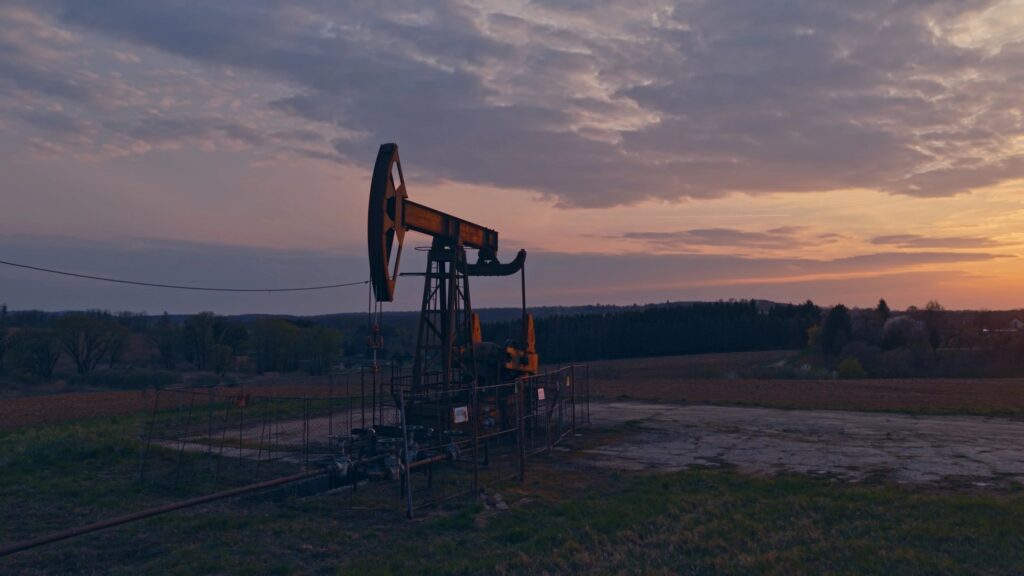 Oil Pump Jack Operating in Rural Field During Dramatic Sunset Sky Showing Traditional Energy Extraction Landscape